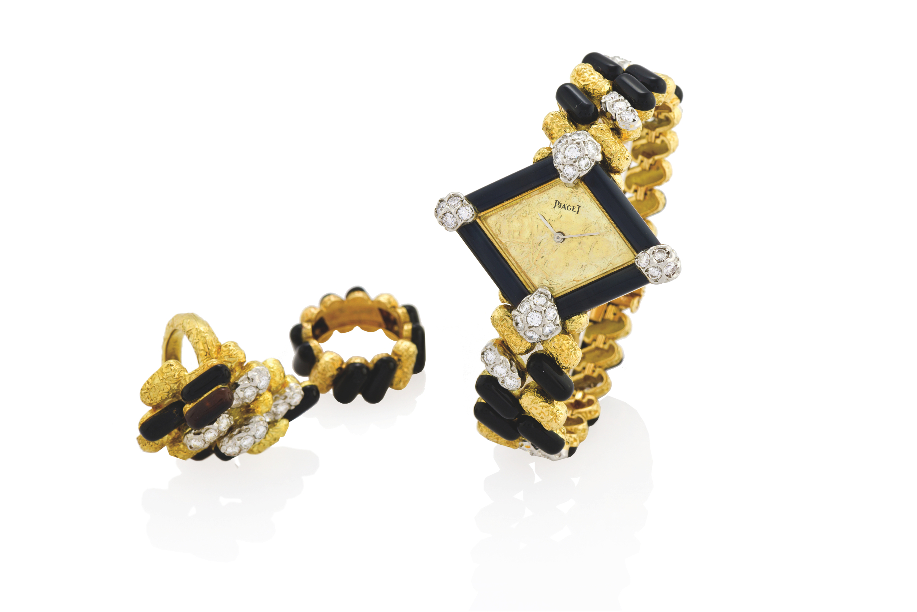 PIAGET YELLOW GOLD, ONYX & DIAMOND
HAUTE JOAILLERIE BRACELET WATCH & TWO RINGS SET
Piaget, Swiss, ?Haute Joaillerie Création?, movement No. 7409568, case No. 551695, Ref. 98212 L14. Made in the 1970s.
Very fine and elegant, lozenge-shaped, 18K yellow and white gold, diamond and black onyx-set lady?s bracelet watch with an integral textured 18K yellow gold, onyx and diamond-set matching bracelet with concealed clasp, set with a total of 52 brilliant cut white diamonds. Accompanied by two rings
